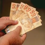Mãos segurando notas de 50 reais, ilustrando o tempo de cessão de precatório.